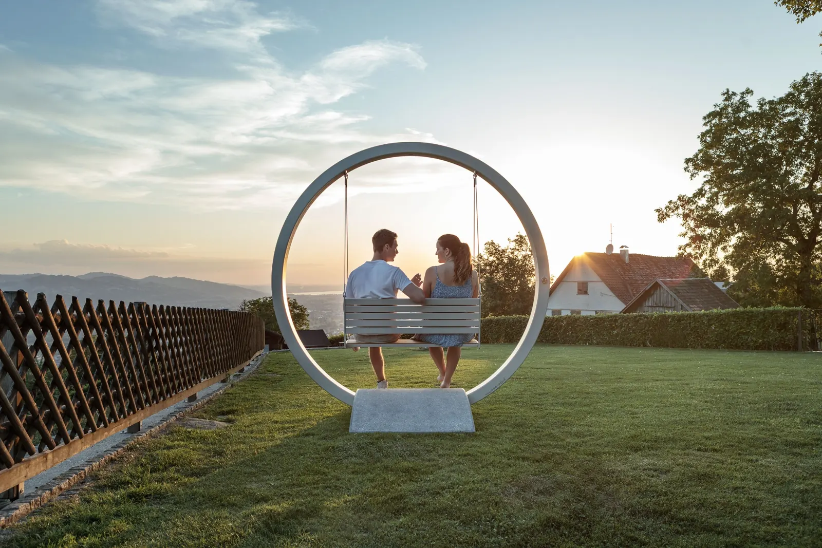Paar auf der oona circle Schaukelbank im Sonnenuntergang